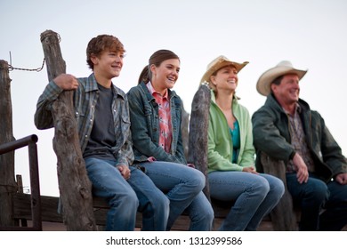 Smiling Family Sitting On A Stable Fence At A Ranch.