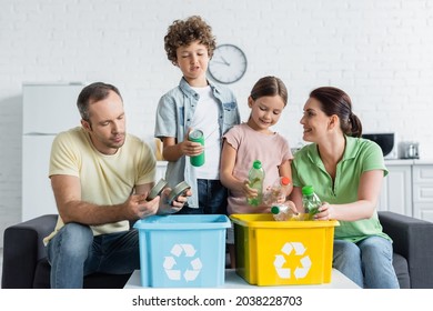 Smiling family sorting trash together in boxes with recycle symbol - Powered by Shutterstock