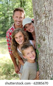 Smiling Family Standing Behind A Tree