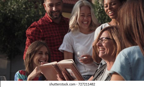 Smiling Family Standing Together While Watching Photos In Album.