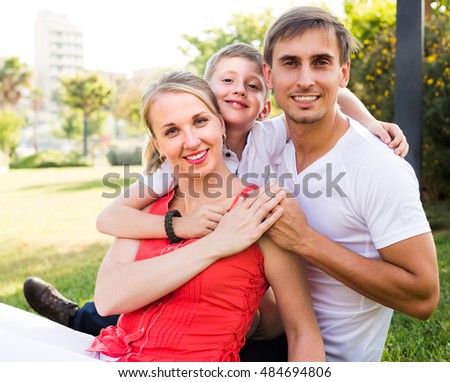 smiling family of three together on green meadow in town on summer day 
