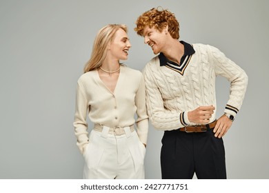 smiling and fashionable couple looking at each other on grey backdrop, timeless classic fashion - Powered by Shutterstock