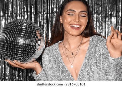 Smiling fashionable woman in sparkling dress with disco ball against silver tinsel Stockfoto