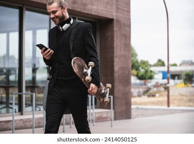 Smiling fashionable young man holding cell phone and skateboard passing office building - Powered by Shutterstock