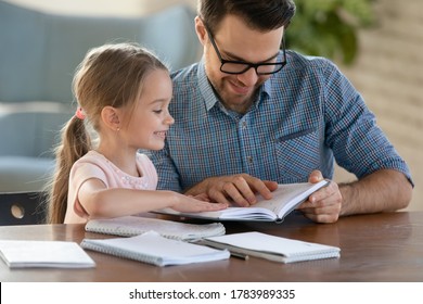 Smiling Father Helping Little Daughter With School Homework, Preparing For Lesson, Studying At Home, Sitting At Work Desk, Caring Dad Checking Tasks, Reading Book, Homeschooling Concept