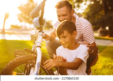 Smiling father and his son having fun together at the green park, fixing bicycle together Stock Photo