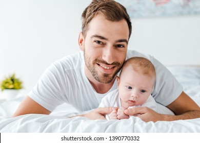 Smiling Father Lying On Bed With Baby In Bedroom