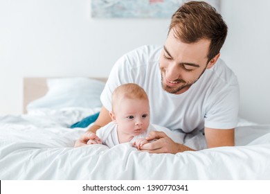 Smiling Father Lying On Bed With Baby In Bedroom