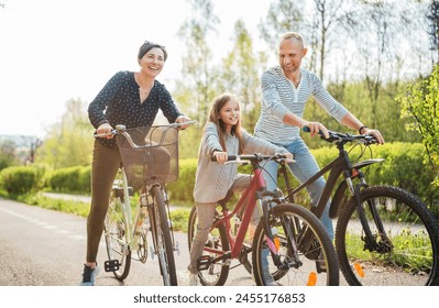 Smiling father and mother with daughter during summer outdoor bicycle riding. They enjoy togetherness in the summer city park. Happy parenthood and childhood or active sport life concept image. - Powered by Shutterstock