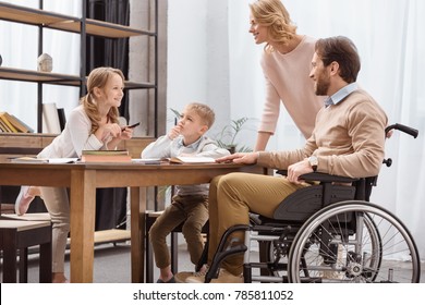 Smiling Father On Wheelchair And Mother Teaching Children At Home