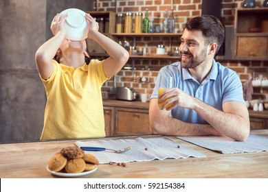 Smiling father with orange juice looking at son eating breakfast from bowl - Powered by Shutterstock