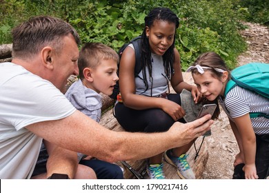 Smiling father showing his two children and a friend pictures on his cellphone during a hike together in a forest - Powered by Shutterstock