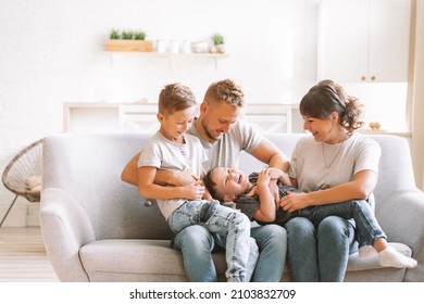 Smiling father sitting on sofa with happy wife and little children and brothers. Excited parents look at children. Happy family with two sons playing at home. The family is sitting on the couch - Powered by Shutterstock