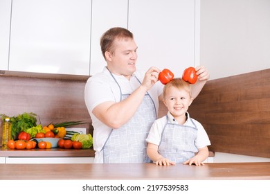 Smiling Father And Son Having Fun Holding Red Bell Peppers In The Form Of Ears, By Dad And Son The Concept Of Cooking On A Day Off, Father's Day