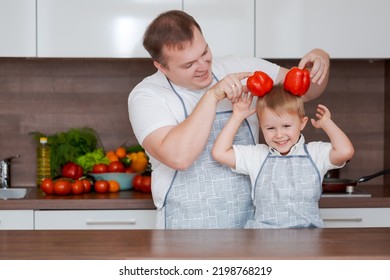 Smiling Father And Son Having Fun Holding Red Bell Peppers In The Form Of Ears, By Dad And Son The Concept Of Cooking On A Day Off, Father's Day