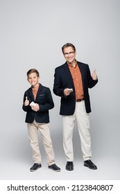 Smiling father and son holding smartphones and showing like on grey background