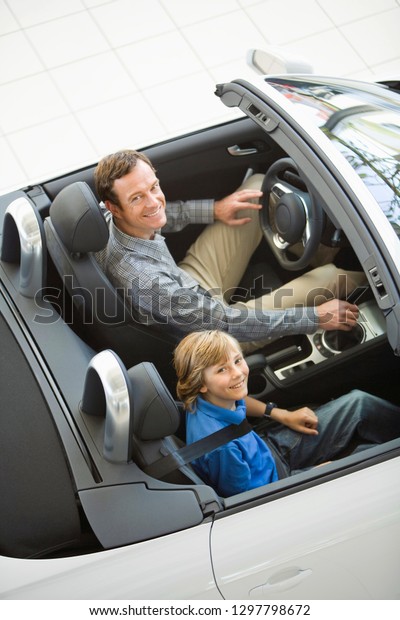 Smiling father and son in showroom sitting in new\
car at camera