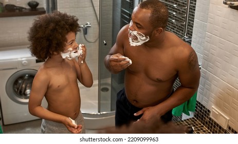 Smiling Father And Son Smearing Faces With Shaving Foam At Home Bathroom. Domestic Family Lifestyle. Black Man And Child Enjoy Time Together. Fatherhood And Parenting. Morning. Hygiene And Face Care