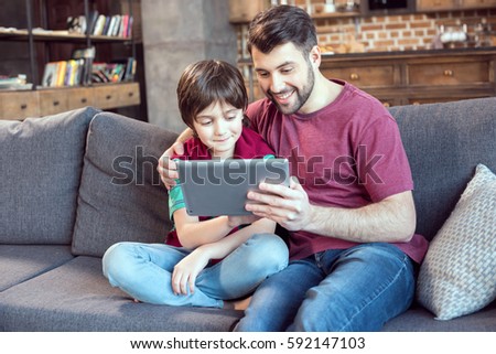 smiling father and son using digital tablet at home