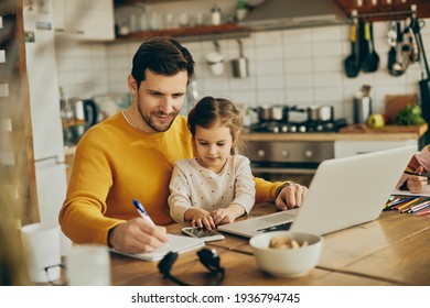 Smiling father working at home while daughter is sitting on his lap.