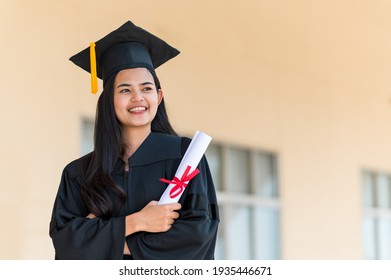 Smiling Female Asian Student In Academic Gown And Graduation Cap Holding Diploma