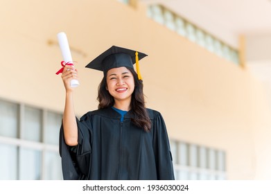 Lächelnde asiatische Studentin im akademischen Gewand und Abitur mit Diplom