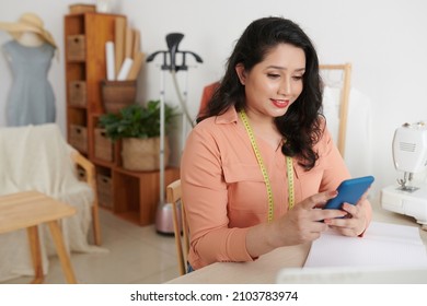 Smiling female atelier manager checking messages from clients on social media - Powered by Shutterstock