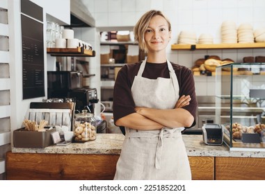 Smiling female baker entrepreneur standing at the counter of bakery and coffee shop. Young woman in cafe near showcase with fresh croissants and bread. Local small business owner indoors. - Powered by Shutterstock