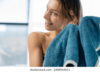 Smiling female with bare shoulders, drying short hair with blue towel after showering. Portrait of cute caucasian woman using towel on wet head in bathroom, with copy space. Concept of hair care. - Powered by Shutterstock