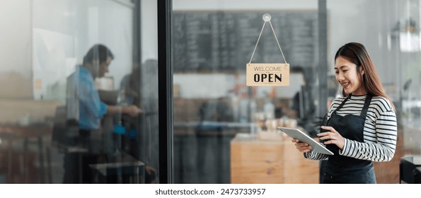 Smiling female barista using a digital tablet in a modern coffee shop with an open sign on the glass door. Busy cafe interior, small business concept. - Powered by Shutterstock