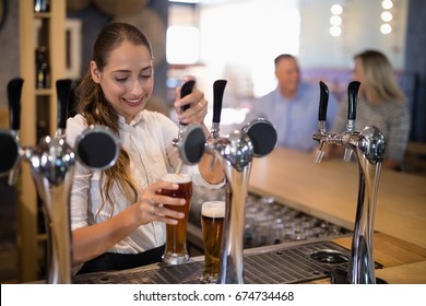 Smiling Female Bartender Filling Beer From Bar Pump At Bar Counter