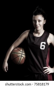 Smiling female basketball player holding ball, in black background