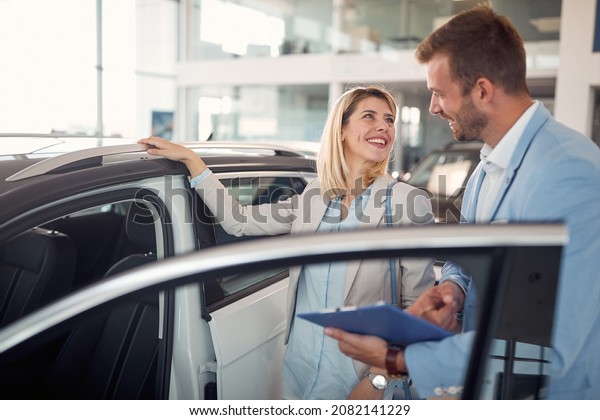 Smiling female in car showroom with car seller buying\
new car