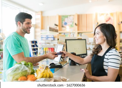 Smiling female cashier with buyer at checkout counter in grocery store