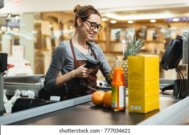 Smiling female cashier scanning grocery items at supermarket