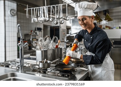 Smiling female chef in hotel or restaurant kitchen cooking and seasoning the food with a pepper or salt mill - Powered by Shutterstock