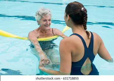 Smiling female coach helping senior woman in swimming pool - Powered by Shutterstock