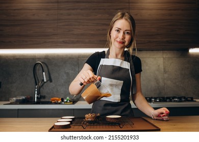 Smiling Female Confectioner Pouring Liquid Chocolate Gommage On Biscuit Cake. Woman Chef In Uniform At Assembling Mousse Dessert Process