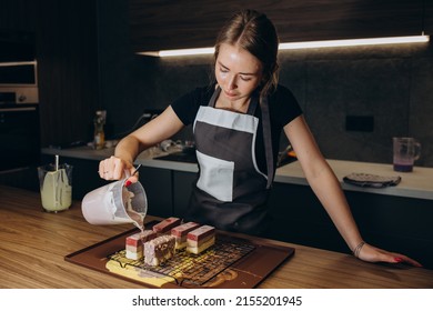 Smiling Female Confectioner Pouring Liquid Chocolate Gommage On Biscuit Cake In Metal Form Working At Catering Service Restaurant. Woman Chef In Uniform At Assembling Mousse Dessert Process