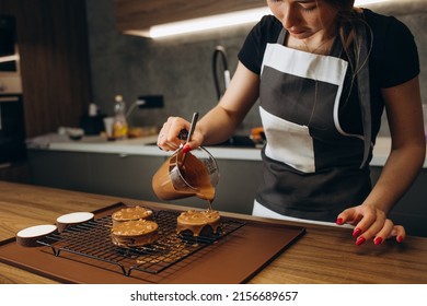 Smiling Female Confectioner Pouring Liquid Chocolate Gommage On Biscuit Cake. Woman Chef In Uniform At Assembling Mousse Dessert Process