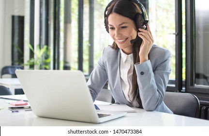 Smiling female customer support operator talking with client and using laptop in office - Shutterstock ID 1470473384