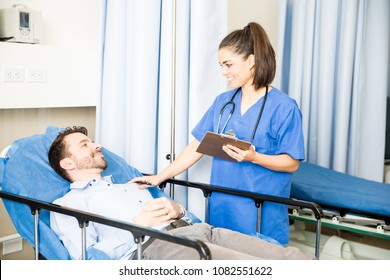 Smiling Female Doctor With A Clipboard Standing Next To A Hospital Bed And Talking With Male Patient