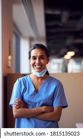 Smiling Female Doctor With Face Mask Wearing Scrubs In Busy Hospital During Health Pandemic