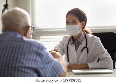 Smiling Female Doctor In Facemask Shake Hand Of Old Male Patient Close Health Insurance Deal In Hospital. Happy Woman GP In Facial Mask Handshake Mature Man Greet Get Acquainted. Healthcare Concept.