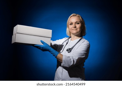 Smiling Female Doctor Holding White Boxes In Her Hands On Dark Background