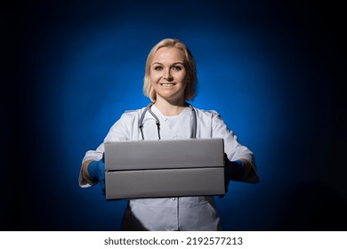 Smiling Female Doctor Holding White Boxes In Her Hands On Dark Background