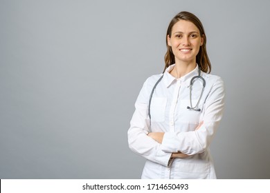 Smiling female doctor in lab coat with arms crossed over gray background - Powered by Shutterstock