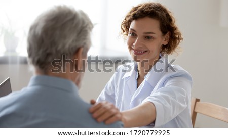 Smiling female doctor reassuring supporting senior adult patient in hospital. Kind caring young woman nurse or caregiver helping older retired man talking, giving comfort, expressing care concept.