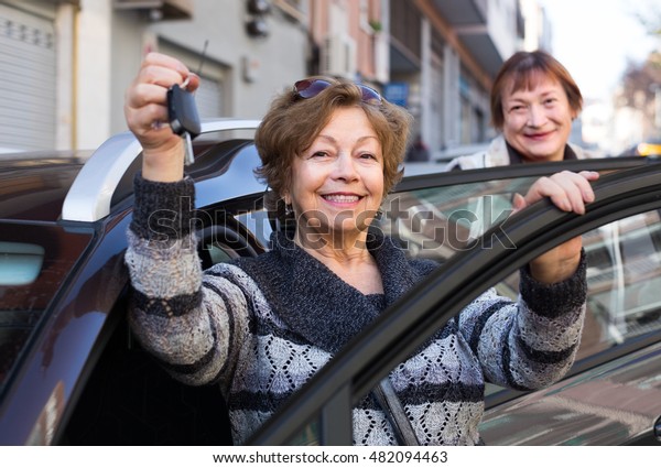 smiling female driver in golden age standing with\
car key outdoor