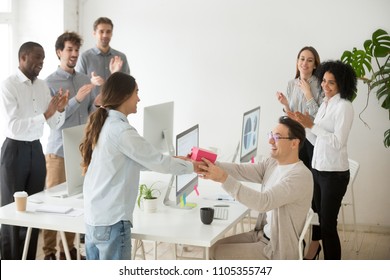 Smiling female employee congratulating colleague with birthday, presenting gift box, diverse coworkers greeting happy male manager, applauding and making unexpected surprise in office - Shutterstock ID 1105355747
